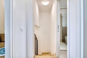 A narrow hallway with a staircase leading to a bathroom with patterned tiles.