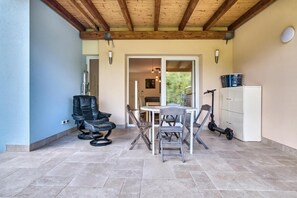 A covered patio area with a table and chairs, a black leather chair, a white cabinet, and an electric scooter.