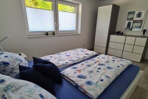 Ein Schlafzimmer mit zwei Betten, einem Fenster mit Jalousien, einem Schrank und einer kleinen Pflanze auf der Fensterbank.