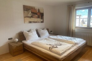 Ein Schlafzimmer mit einem hölzernen Bett, weißer Bettwäsche, einem Nachttisch mit Lampe, einem Bild an der Wand und einem Fenster mit Vorhängen.