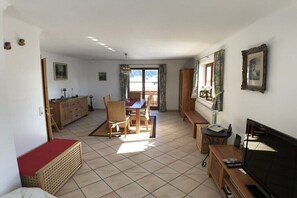 A room with a bed, a TV, a dining table with chairs, a window with curtains, and a wooden cabinet. - Holiday apartment in Krün with Wi-Fi (Krün)