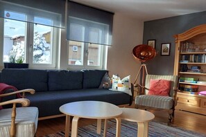 Ein Wohnzimmer mit einer Couch, zwei kleinen Tischen, einer Stehlampe und einem Bücherregal.