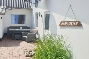 A small outdoor seating area with wicker furniture, a white wall with a sign reading 'KRÄUTERGARTEN,' and a potted plant. - Anchorage time pasture field (Kappeln)