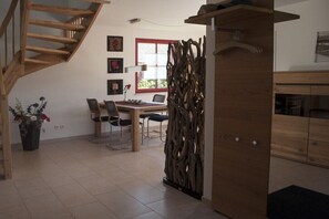 Ein modernes Interieur mit einer Holztreppe, einem Essbereich mit Stühlen und Tisch, einer Wanddekoration und einem Holzschrank.