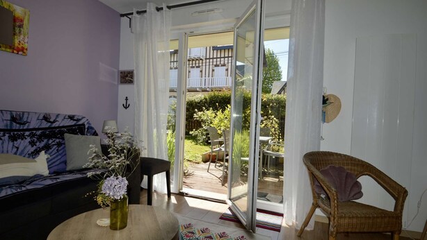 Ein Zimmer mit einer Couch, einem Sessel, einem Tisch mit einer Vase und einer Schiebetür aus Glas zu einem Außenbereich mit einem Balkon.