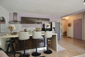 Eine moderne Küche mit einer zentralen Kochinsel, Barhocker, Backofen und Kühlschrank.