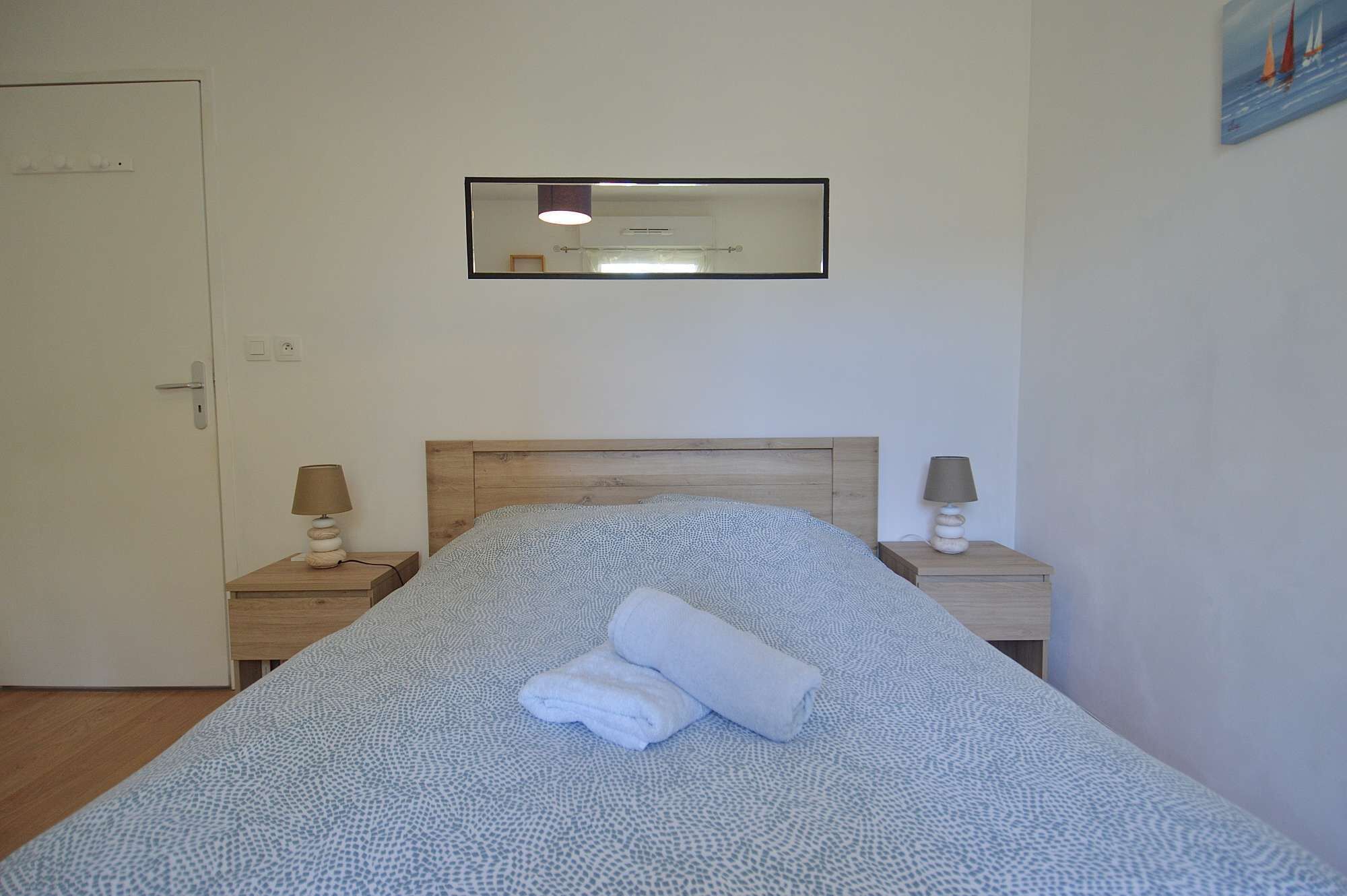 A bedroom with a bed, a bedside table, a nightstand, a mirror, and a painting on the wall.