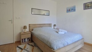 Ein Schlafzimmer mit einem hölzernen Bett, einem Nachttisch mit Lampe, einem kleinen Bücherregal und einem Teppich.
