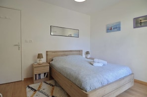 Ein Schlafzimmer mit einem hölzernen Bett, einem Nachttisch mit Lampe, einem kleinen Bücherregal und einem Teppich.