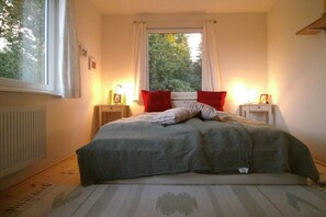 Ein Schlafzimmer mit einem Bett, zwei Nachttischen, einem Fenster mit Vorhängen und einer Heizung.