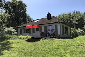 Ein kleines Haus mit Terrasse, einem roten Sonnenschirm und einem Schornstein.