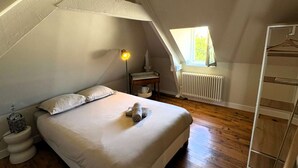 Ett sovrum med ett sluttande tak, en säng med kuddar, ett sängbord med en lampa, ett element och ett fönster som släpper in naturligt ljus.