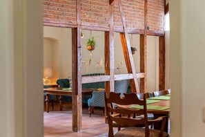 Ein rustikales Interieur mit freiliegenden Ziegelwänden, Holzbalken, einem Esstisch mit Stühlen und einer hängenden Pflanze.