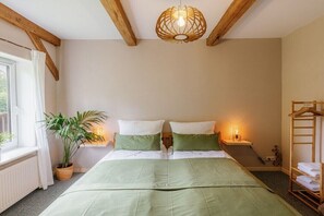 Ein Schlafzimmer mit Bett, Nachttischen, einer Hängelampe, einem Fenster mit Vorhängen und einer Pflanze.
