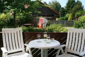 Eine Terrasse mit zwei weißen Stühlen, einem runden Tisch und einer Weinflasche.