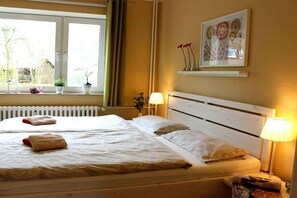 Ein Doppelbett mit weißen Leinen, eine Nachttischlampe und ein Fenster mit Vorhängen.