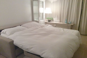 A neatly made bed in a hotel room with a bedside table, a lamp, and a window with curtains. - Holiday apartment in Laboe with swimming pool (Laboe)