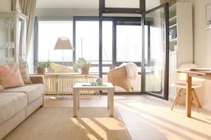 A modern living room with a sofa, a coffee table, and a chair. There is a large window with a view of the outside. - Holiday apartment in Laboe with swimming pool (Laboe)