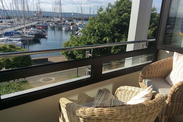 A balcony with wicker furniture overlooking a marina with boats. - Holiday apartment in Laboe with swimming pool (Laboe)