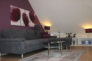 A modern living room with a grey sofa, a glass coffee table, and a large abstract painting on the wall. - Holiday home in Röbel with swimming pool (Röbel)