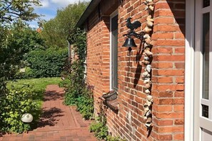 Ein Backsteinhaus mit einem Weg, der zu einem Fenster führt, umgeben von Grünpflanzen.