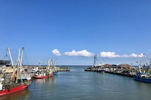 Ein Hafen mit mehreren vor Anker liegenden Fischerbooten, einer sich ins Wasser erstreckenden Mole und Gebäuden im Hintergrund.