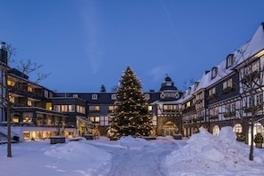 Ein verschneiter Innenhof mit Weihnachtsbaum, traditioneller europäischer Architektur und blauem Himmel.