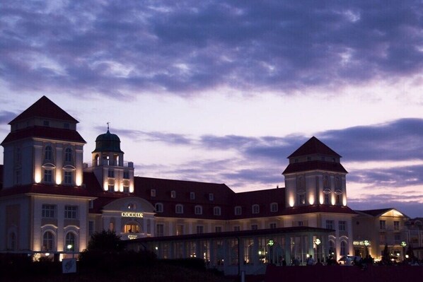Ein historisches Gebäude mit mehreren Türmen und einer zentralen Kuppel, das einen prunkvollen Eingang und eine überdachte Passage besitzt.