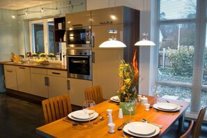 Eine moderne Küche mit integrierten Geräten, einem Esstisch für vier Personen und einem großen Fenster mit Jalousien.