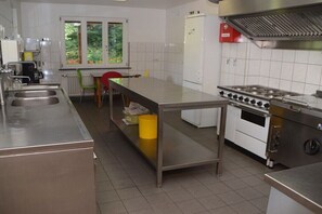 Ett professionellt kök med rostfria köksmaskiner, ett stort bord och ett fönster med utsikt över grönområden.