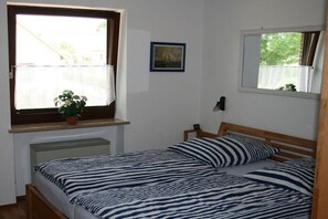 A bedroom with a single bed, a window with lace curtains, a small potted plant, and a framed picture on the wall. - Water chicks at the boat dock (Kosel-Missunde)