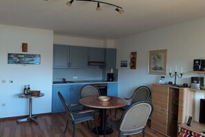 A compact kitchen with blue cabinets, a dining table with four chairs, a small side table, and a cabinet with a radio and candles. - Water chicks at the boat dock (Kosel-Missunde)