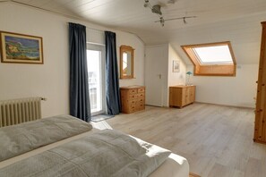 Ein Schlafzimmer mit Bett, Kommode, Spiegel, Oberlicht und einem Gemälde an der Wand.