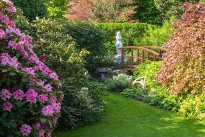 Ein Garten mit einer Statue, einer Holzbrücke und üppigem Grün.