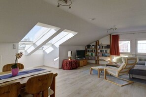 Un salon avec une lucarne, un téléviseur, une bibliothèque, un canapé et une table à manger avec des chaises.