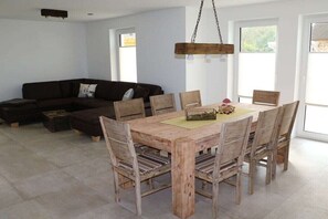 A dining area with a wooden table and chairs, a black sofa, and a hanging light fixture. - Holiday home in Mellnitz with swimming pool (Mellnitz)