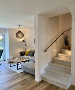 Ein modernes Wohnzimmer mit Treppe, Sofa, Couchtisch und einer Pendelleuchte.