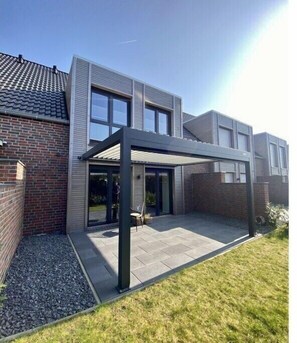 Ein modernes Haus mit einer überdachten Terrasse, einer Ziegelwand und einem gepflegten Rasen.