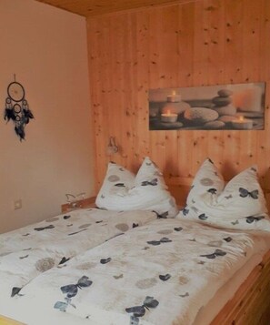 Une pièce en bois avec un lit, des oreillers, un attrape-rêves et un tableau représentant des bougies.