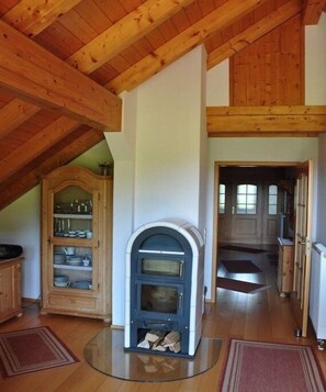 Ein rustikales Interieur mit Holzbalkendecke, eingebautem Holzofen, einem Schrank mit Geschirr und einer Tür zu einem anderen Raum.