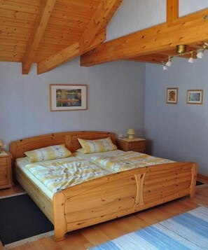 Ein hölzernes Bett in einem Raum mit schrägen Wänden und gerahmten Bildern.