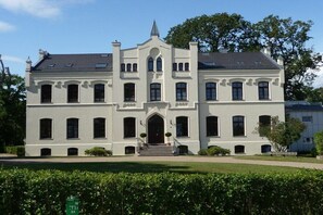 Ein großes, weißes Gebäude mit zwei Stockwerken, einer symmetrischen Fassade, zahlreichen Fenstern und einem zentralen Eingang mit Stufen.