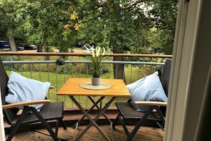 Eine Terrasse mit Tisch und zwei Stühlen, umgeben von einem Metallgeländer.