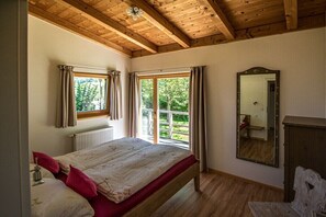 Ein Schlafzimmer mit Holzboden, einem Bett mit Blumenmuster auf der Bettwäsche, einem Fenster mit Vorhängen und einem Spiegel.