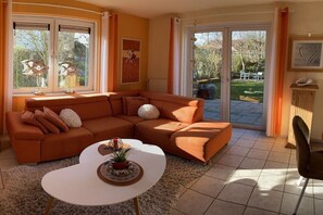 Ein Wohnzimmer mit einer Eckcouch, einem weißen Couchtisch und Blick auf den Garten durch große Schiebetüren.