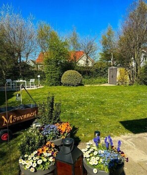Ein Garten mit Blumenbeeten, einem hölzernen Wagen und einem Gartenhaus.