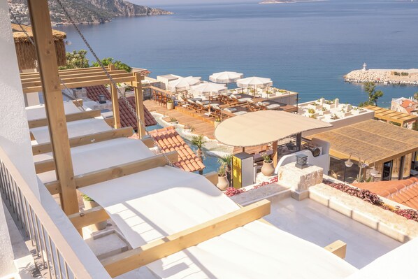 A rooftop terrace with a pool, sun loungers, umbrellas, and a view of the sea.