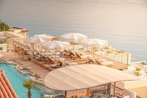 A rooftop pool area with lounge chairs and umbrellas, overlooking a body of water.