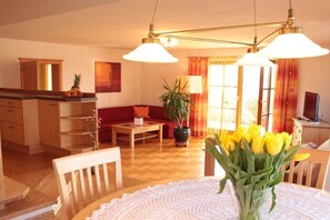 A living room with a sofa, a coffee table, a dining table with chairs, a potted plant, and a vase of flowers. - Quiet holiday apartment with lake view (Eggelsberg)
