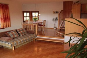 A cozy living room with a sofa, dining table, chairs, and a staircase leading to an upper level. - Quiet holiday apartment with lake view (Eggelsberg)
